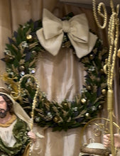 Decorative wreath with a figure in the center, surrounded by greenery and gold accents.